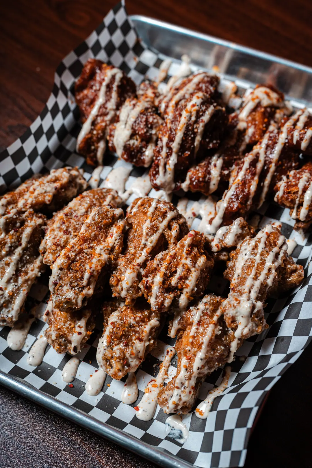 Crispy seasoned chicken wings with a ranch drizzle and chili flakes on checkered paper