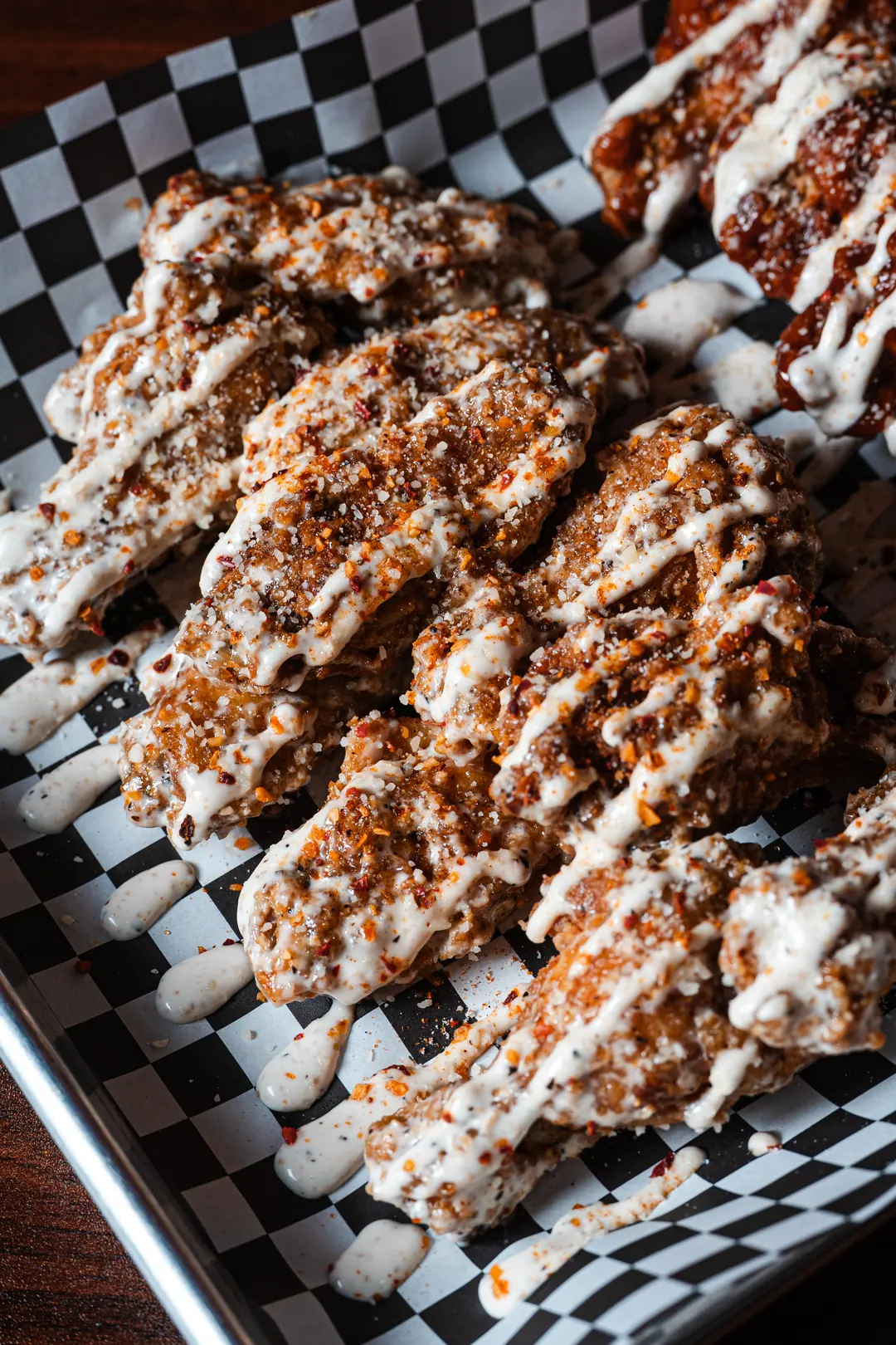 Close-up of dry-rub chicken wings topped with ranch and chili flakes