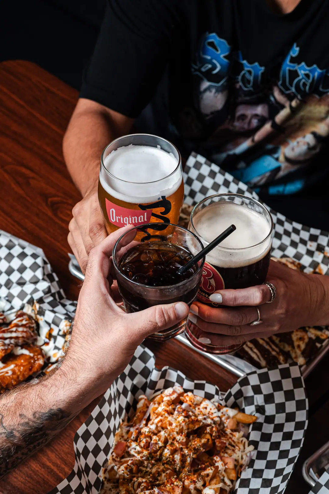 Friends raising drinks over wings and loaded fries at Sauce N Toss in Strathroy