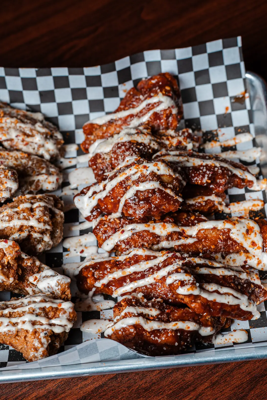 Glazed chicken wings with a ranch drizzle and chili flakes on a metal tray
