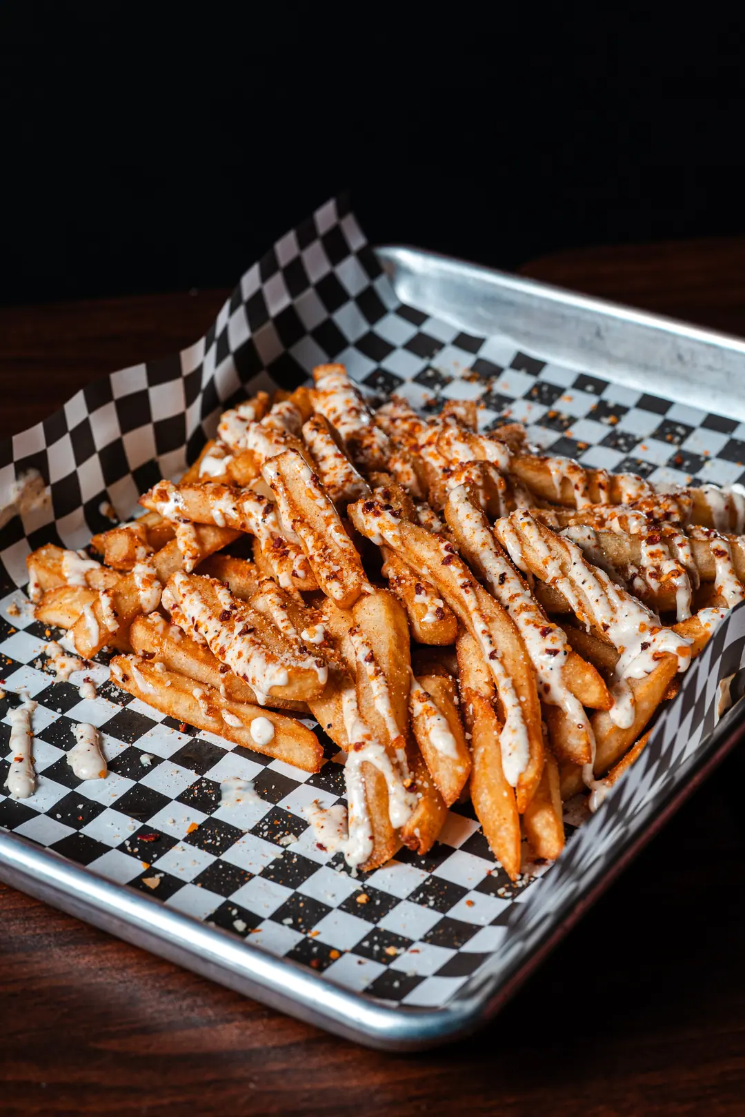 Seasoned french fries with a ranch drizzle in a checkered paper-lined tray